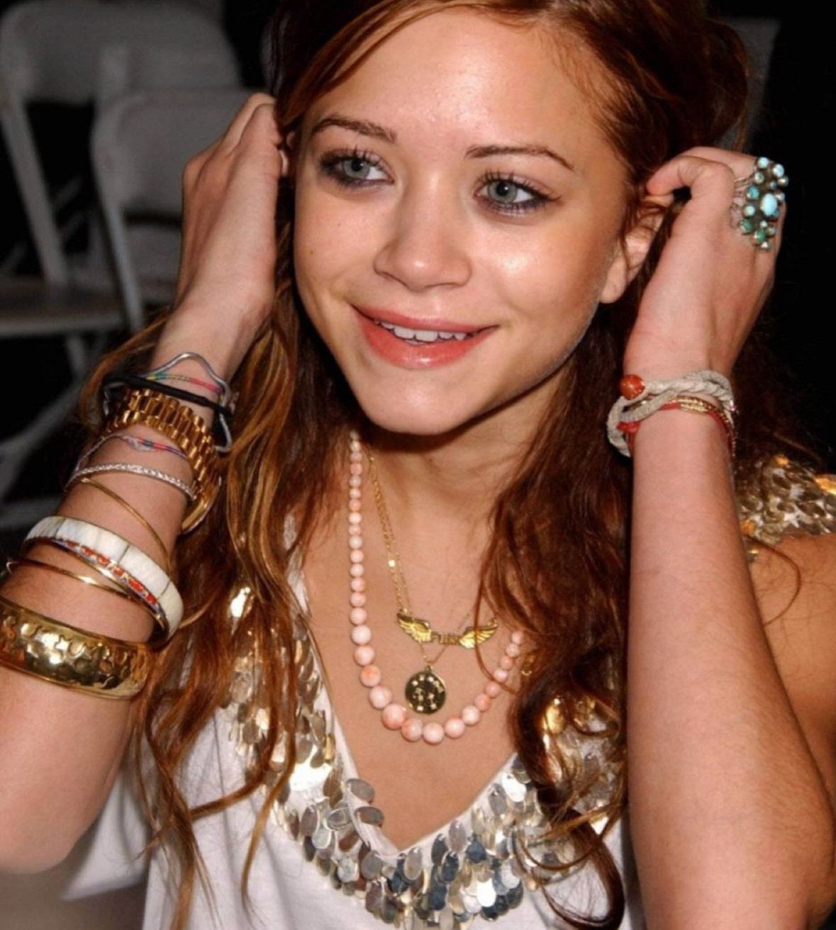 Woman wearing multiple gold bracelets, a beaded necklace, and a large turquoise ring.