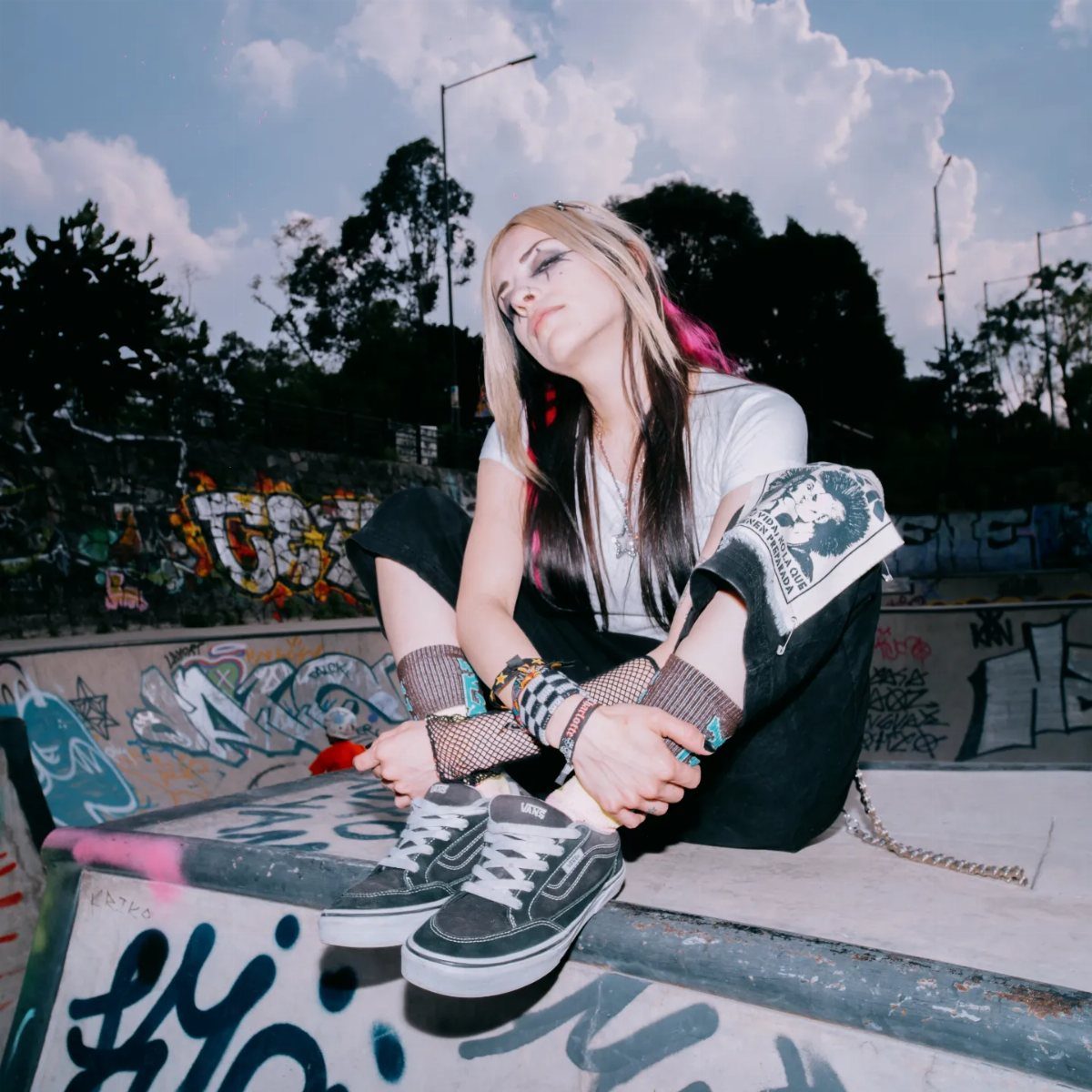 Woman in punk rock fashion sitting on a graffiti-covered concrete skate park ledge.