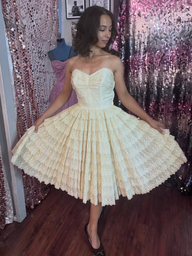 Woman wearing a strapless cream-colored 1950s style party dress with tiered lace skirt