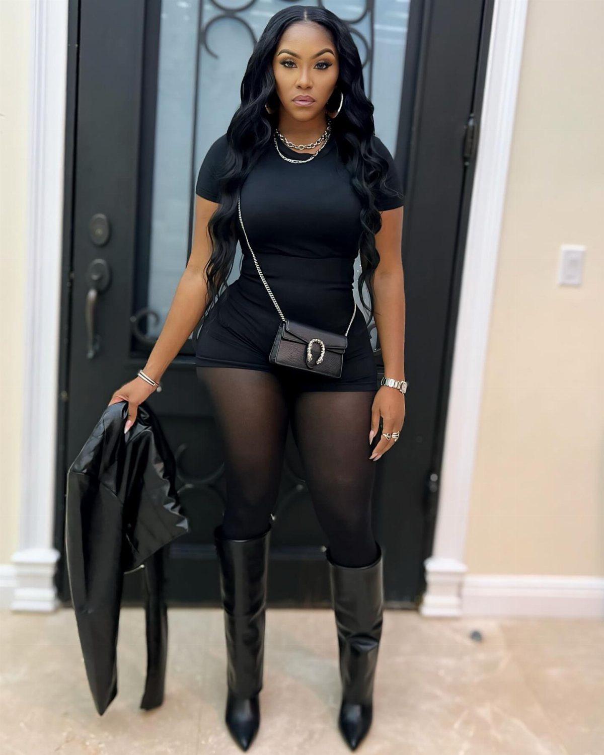 Woman wearing a short black dress, black tights, and black knee-high boots.