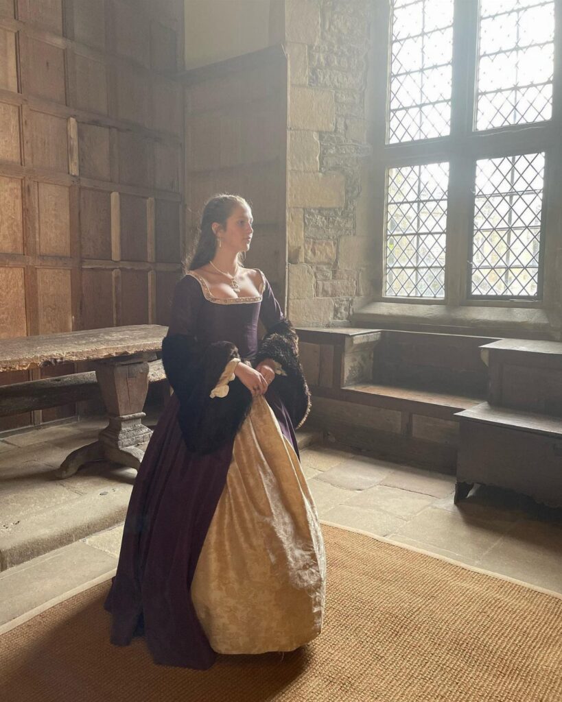 Woman wearing a purple and gold Tudor-style gown in a stone room