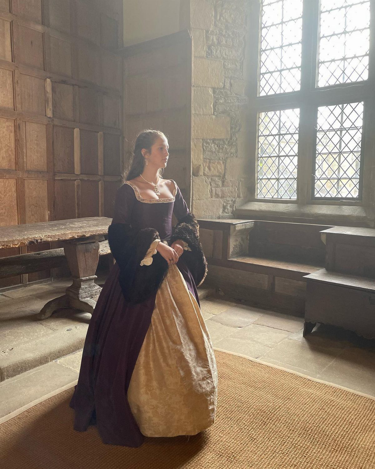 Woman wearing a purple and gold Tudor-style gown in a stone room