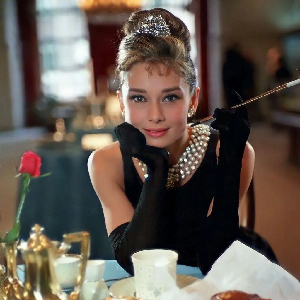 Audrey Hepburn in a black dress, pearls, and tiara holding a cigarette holder.