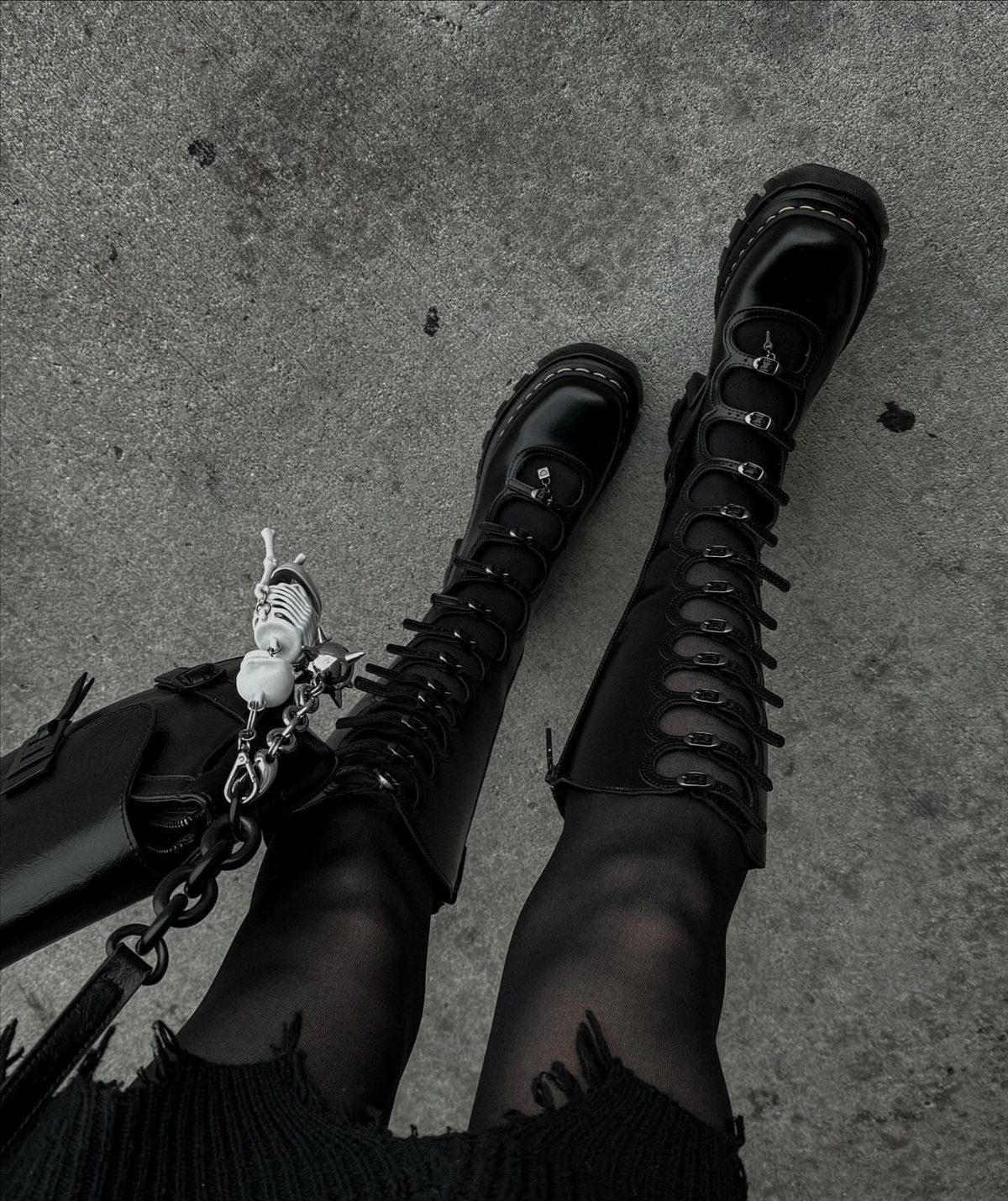 Tall black lace-up platform boots and sheer tights on a concrete ground