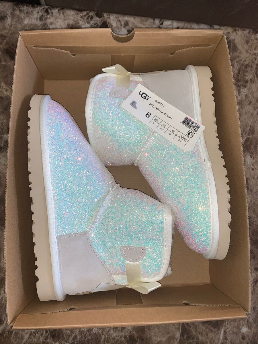 Rhinestone-covered white UGG boots with satin bows inside a brown cardboard shoebox.