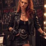 Woman with red hair wearing black leather jacket and skirt with rock accessories.