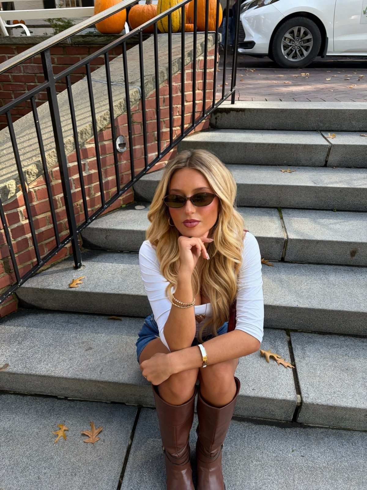 Woman in white top and denim shorts wearing tall brown leather boots.
