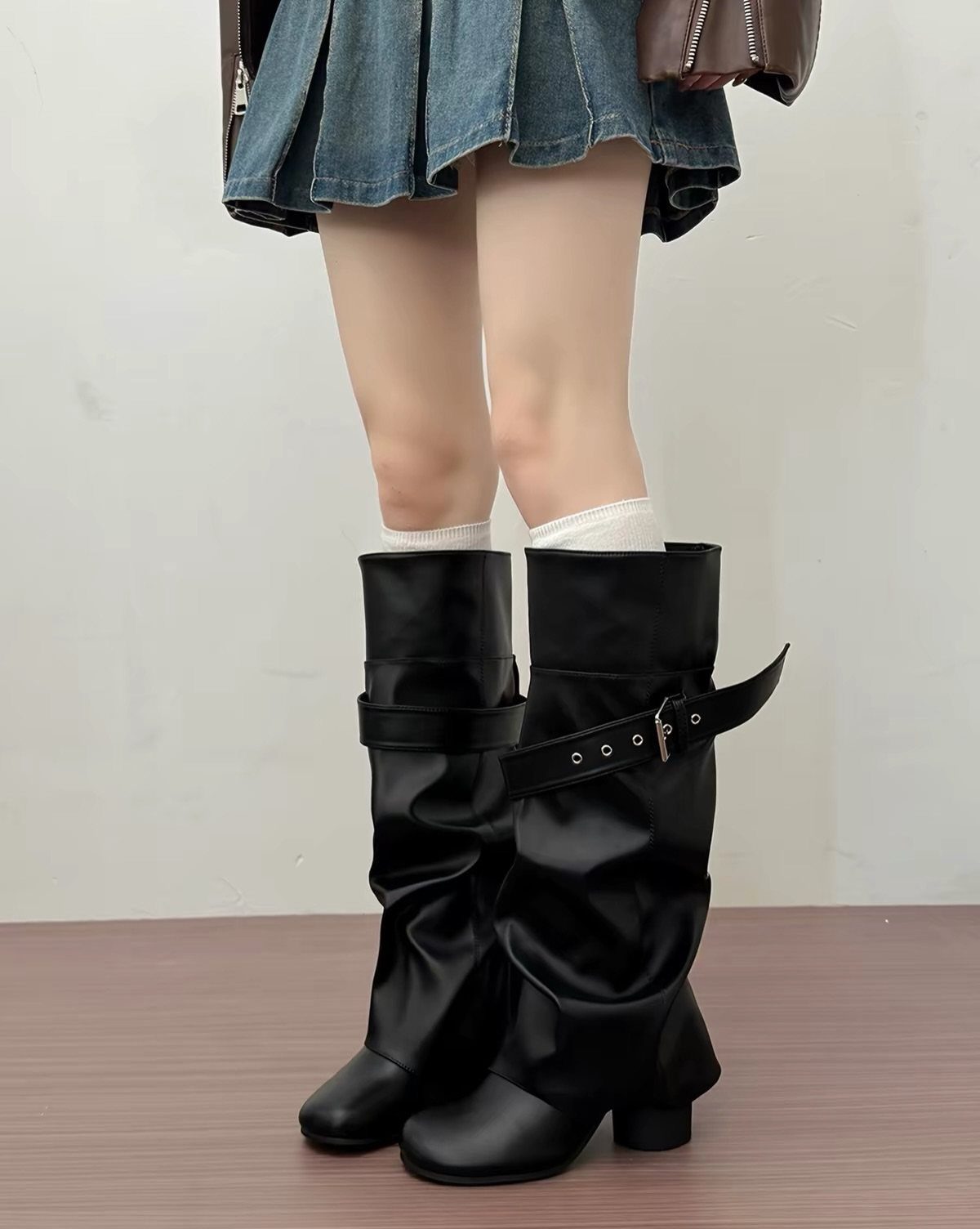 Black slouchy leather boots with silver buckles worn with a denim skirt.