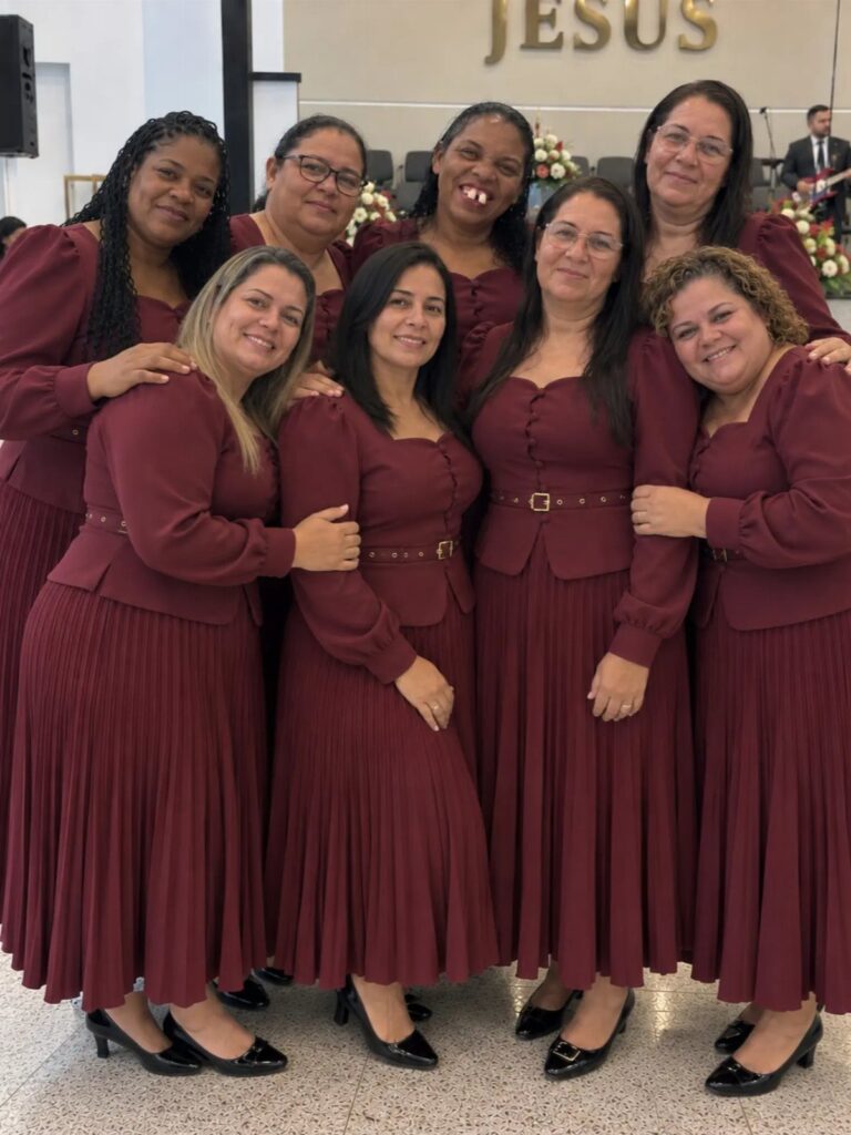 Seven women wearing matching burgundy pleated dresses posing inside a church.