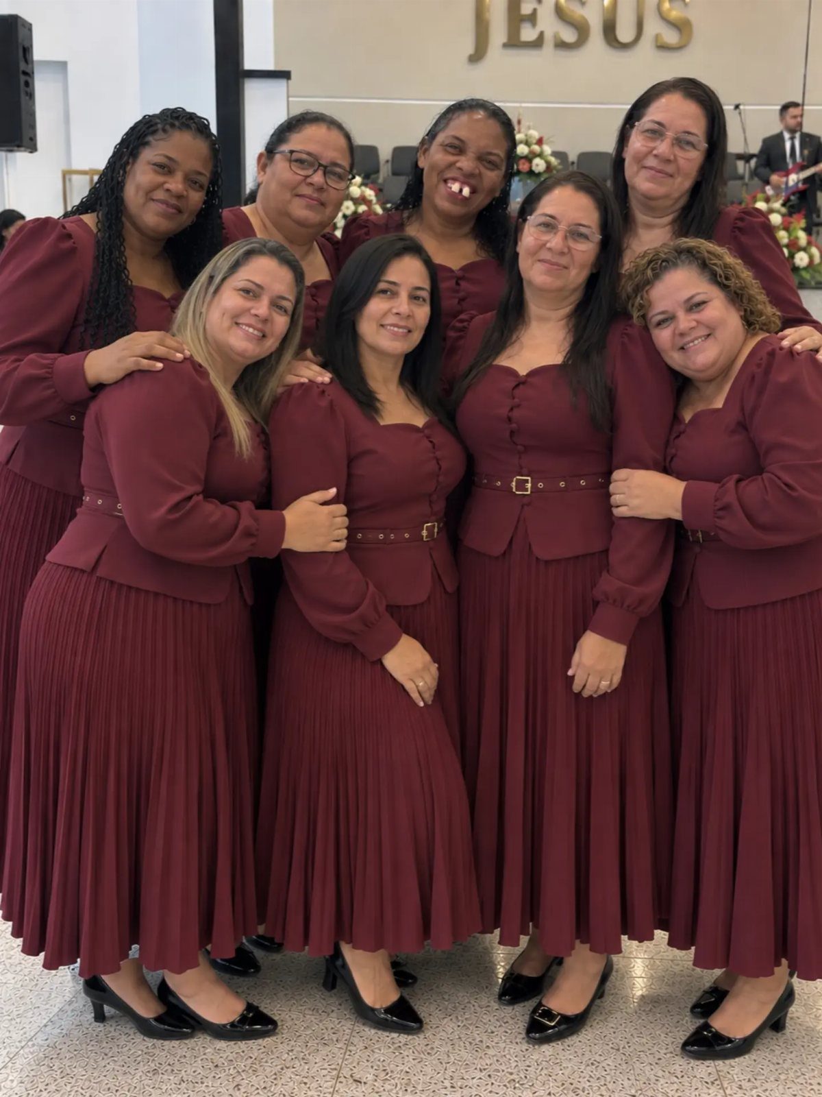 Seven women wearing matching burgundy pleated dresses posing inside a church.