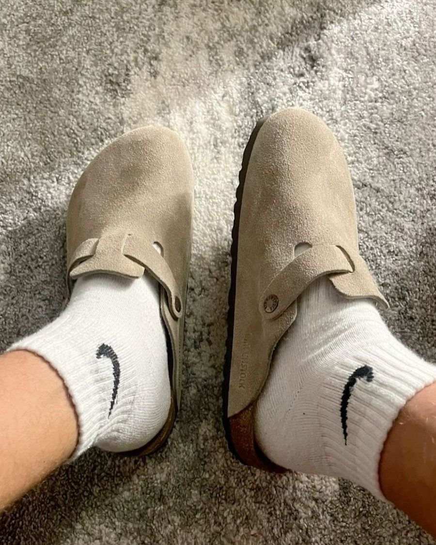 Tan suede clog shoes worn with white Nike socks on grey carpet.