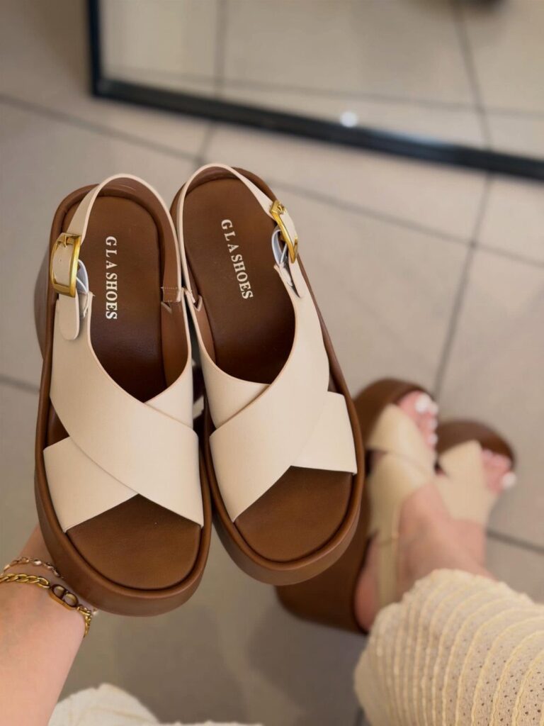 Beige platform sandals with criss-cross straps held up against a tiled floor.