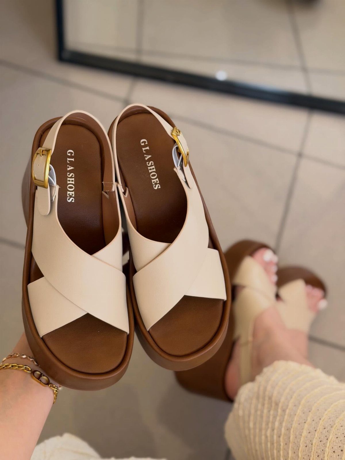 Beige platform sandals with criss-cross straps held up against a tiled floor.