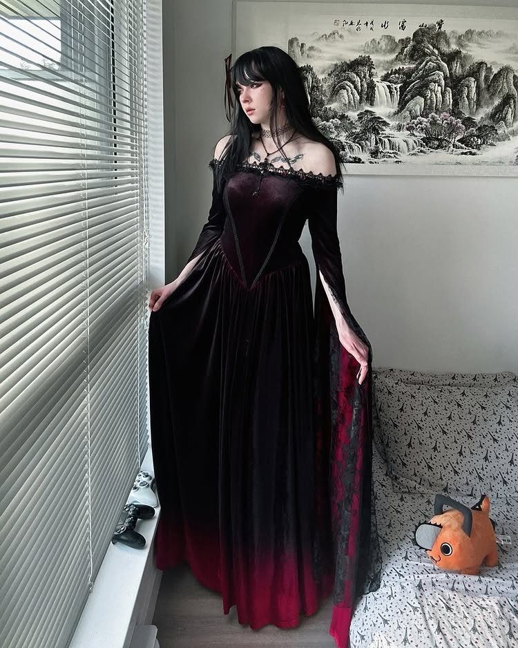 Woman wearing a long burgundy and black velvet goth romantic dress indoors.
