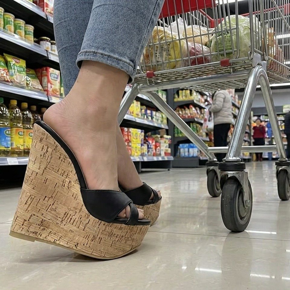 Black open-toe wedge heels with cork soles worn with blue jeans in a store.