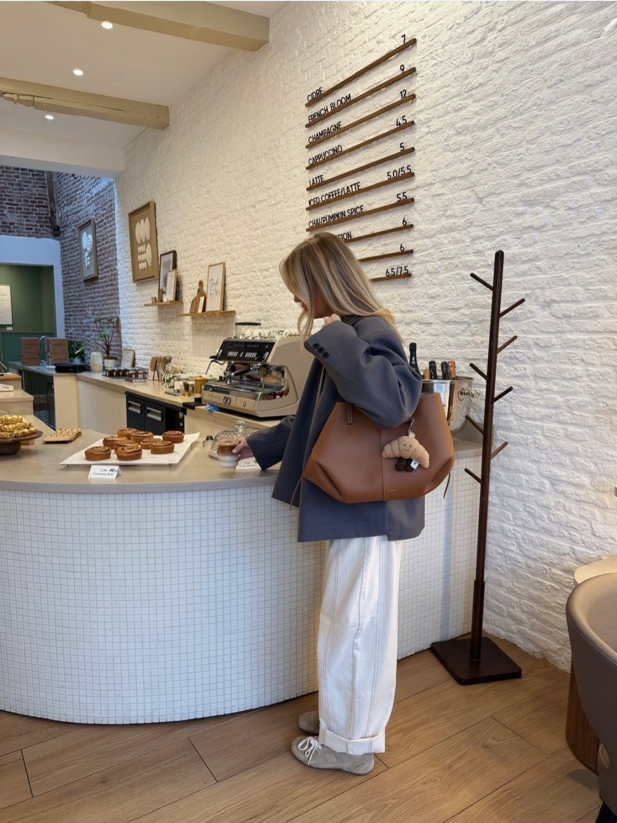 Woman in grey blazer and white baggy jeans standing at a cafe counter