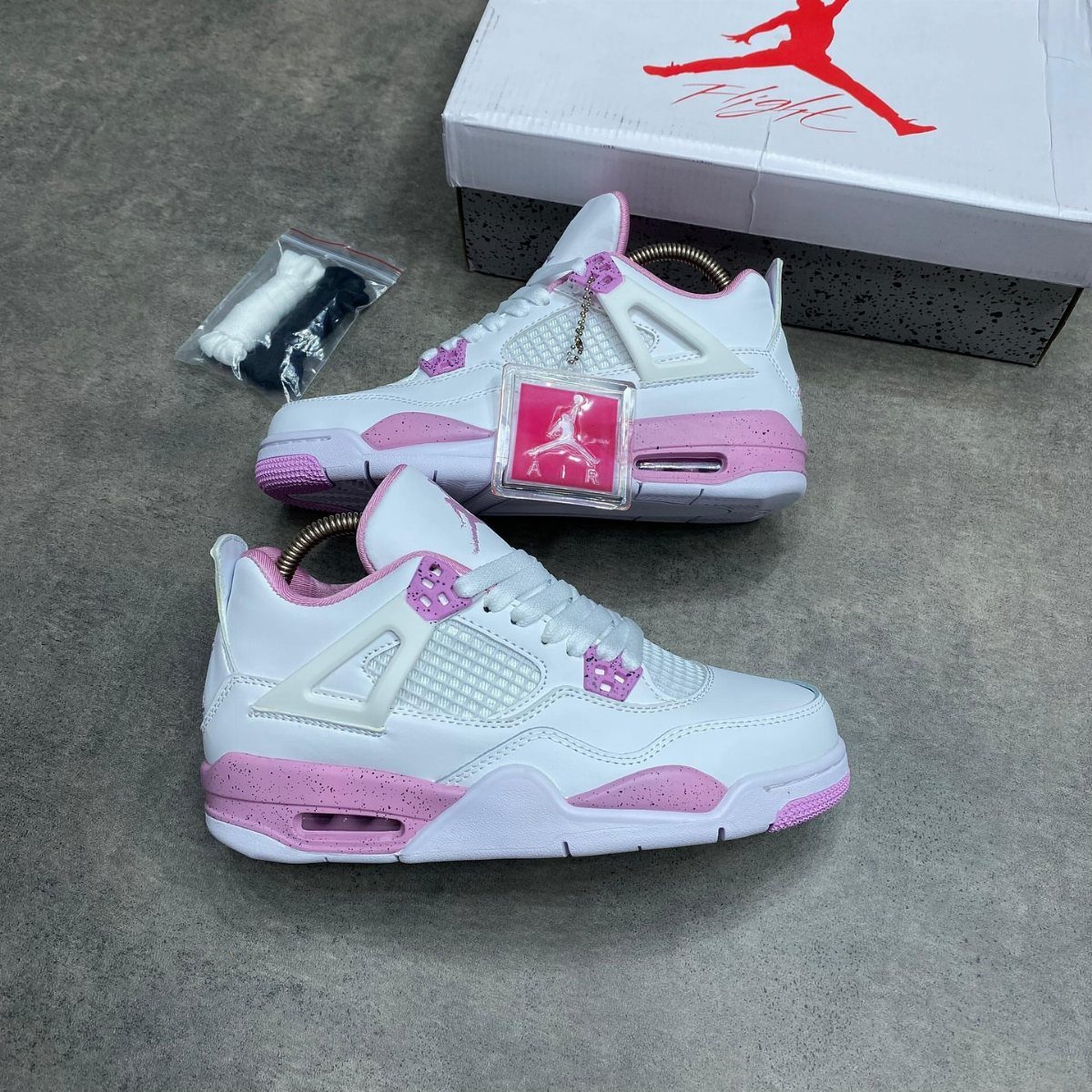 White and pink Air Jordan 4 retro sneakers next to their branded shoe box.