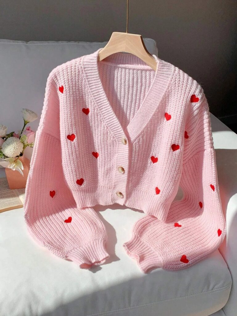 Pink knitted cardigan with red hearts hanging on a wooden hanger over white sofa
