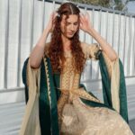 Woman wearing a gold and green medieval theme dress with ornate embroidery.