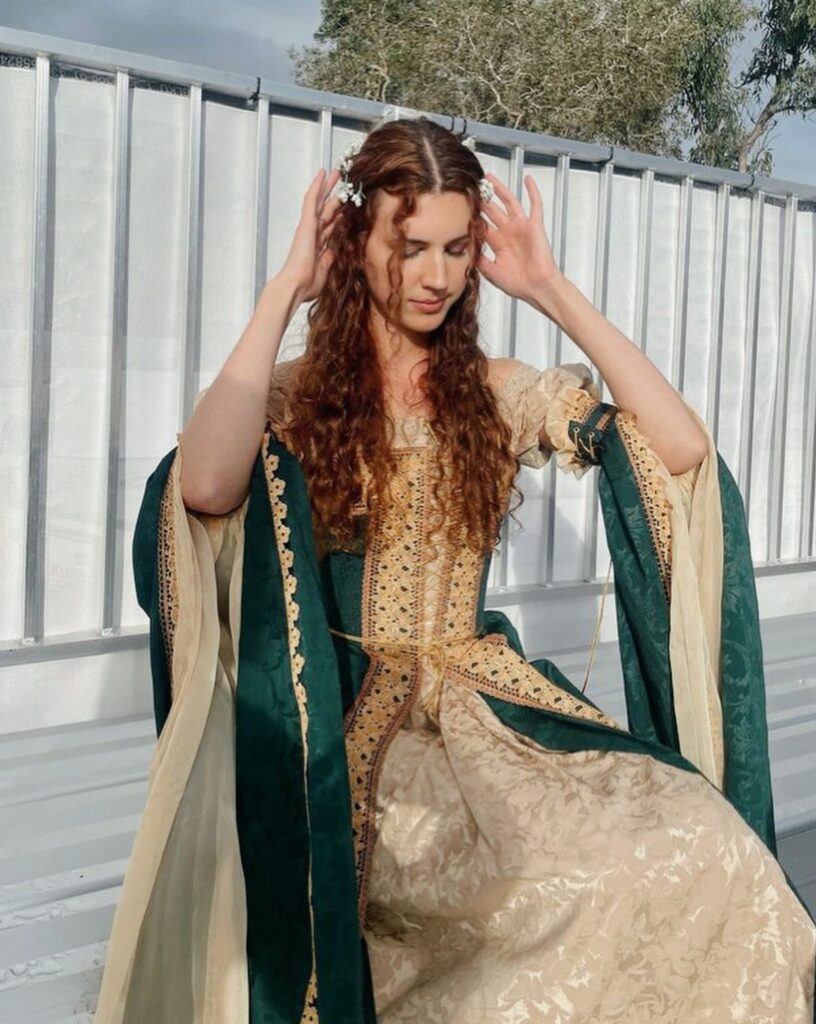 Woman wearing a gold and green medieval theme dress with ornate embroidery.