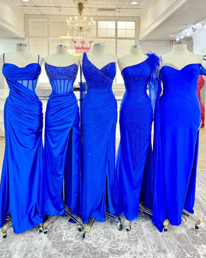 Five royal blue gowns in different styles displayed on mannequins in a boutique.