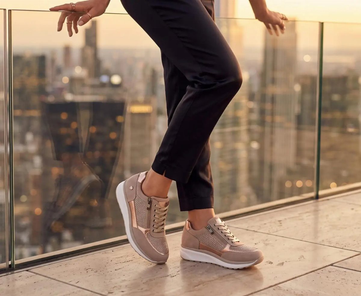 Rose gold metallic sneakers with white soles worn with black trousers on a balcony.
