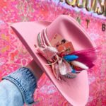 Pink cowboy hat decorated with a sparkly bow and feathers held by a hand.