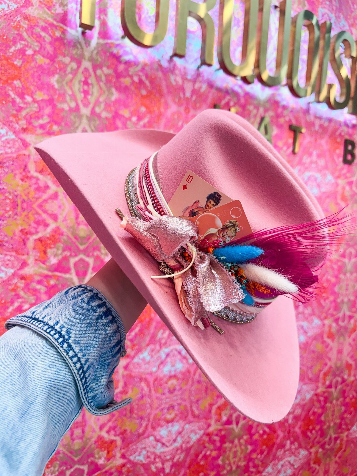 Pink cowboy hat decorated with a sparkly bow and feathers held by a hand.
