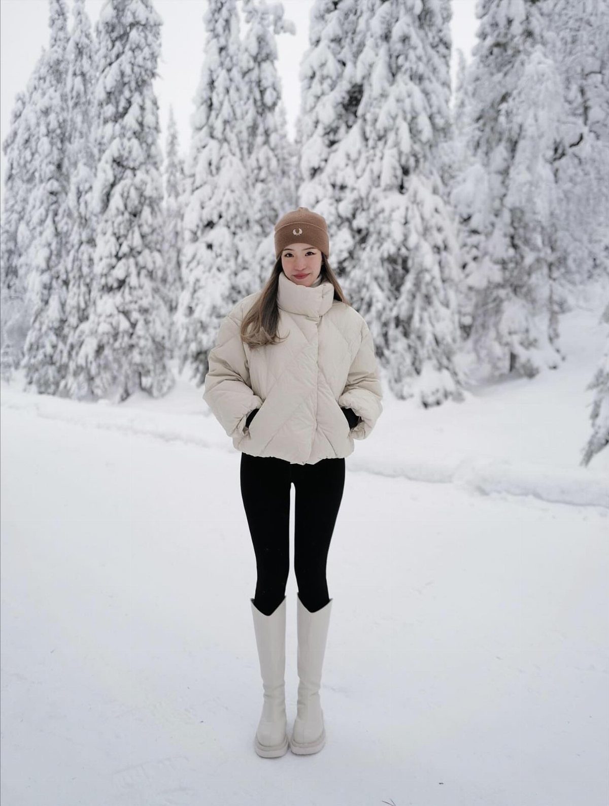 Woman in white puffer jacket and white winter boots standing in snowy forest